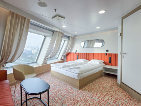 Ein Hotelzimmer mit grossen Fenstern, einem Bett, einem Sofa, Tischchen und Sessel.
