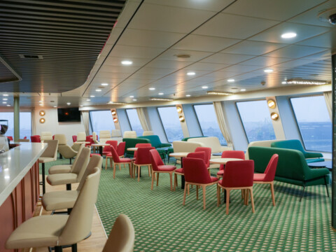 Moderne Lounge im Schiff mit einer Bar, bunten Sitzmöbeln und grossen Fenstern.
