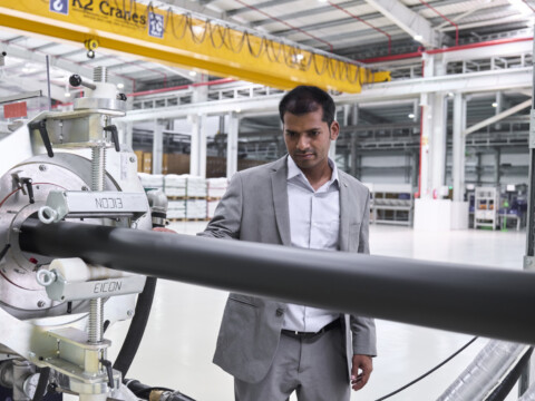 Ein Mann in einem Anzug steht in einer modernen Fabrik und beobachtet eine grosse Maschine mit einem langen, schwarzen Rohr.