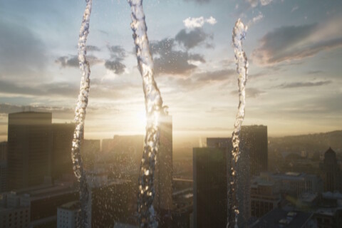 Water streams in front of a city skyline at sunset.