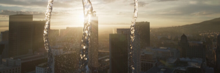 Water streams in front of a city skyline at sunset.