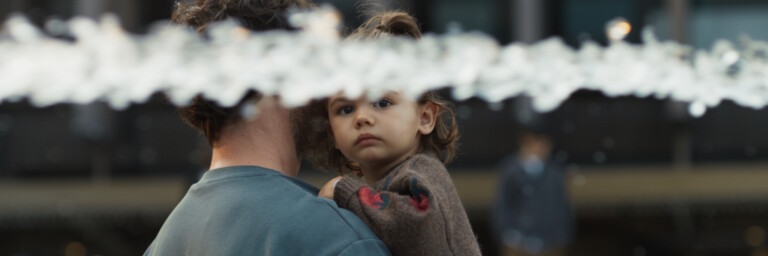 A person holding a child with water splashing in the foreground.