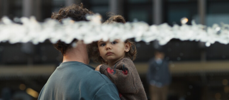 A person holding a child with water splashing in the foreground.
