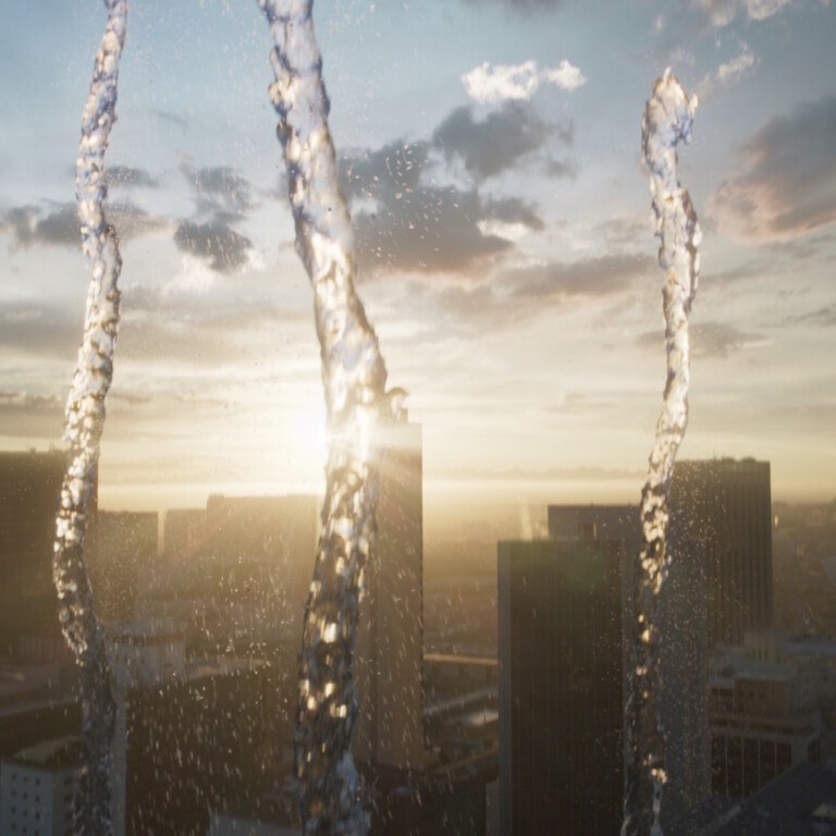 Water streams in front of a city skyline at sunset.
