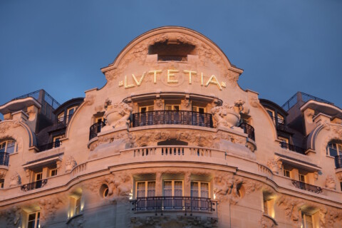 The ornate facade of a historic hotel, featuring the name "Lutetia" in large letters, illuminated against a twilight sky.