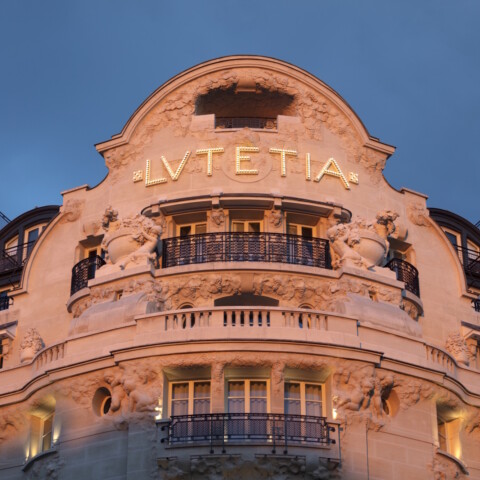 The ornate facade of a historic hotel, featuring the name "Lutetia" in large letters, illuminated against a twilight sky.
