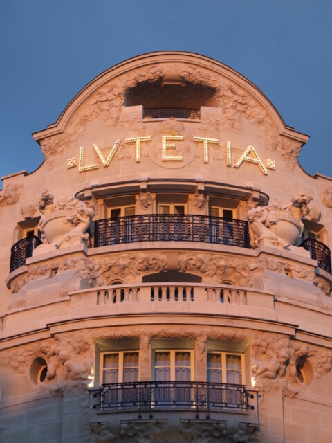 Fassade eines historischen Gebäudes mit dem Schriftzug "Lutetia" und Verzierungen, beleuchtet bei Dämmerung.