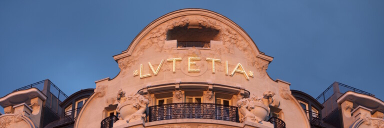 Fassade eines historischen Gebäudes mit dem Schriftzug "Lutetia" und Verzierungen, beleuchtet bei Dämmerung.
