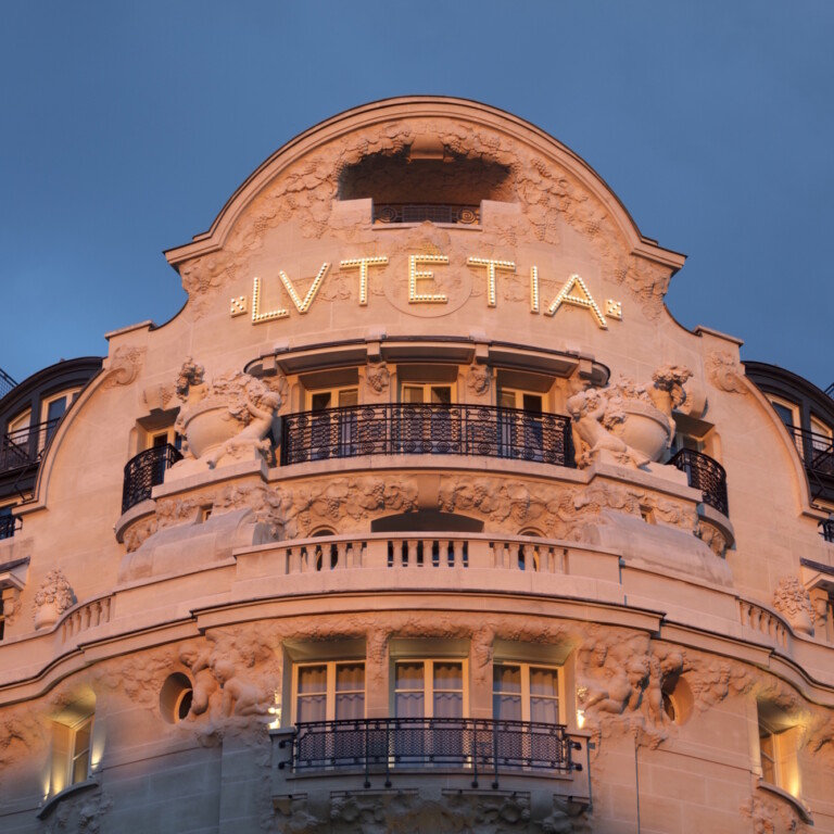 Fassade eines historischen Gebäudes mit dem Schriftzug "Lutetia" und Verzierungen, beleuchtet bei Dämmerung.