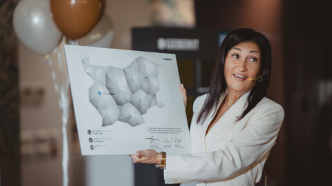 Eine Frau in einem stylischen weissen Anzug hält eine Grafik mit einer Karte in der Hand und lächelt.