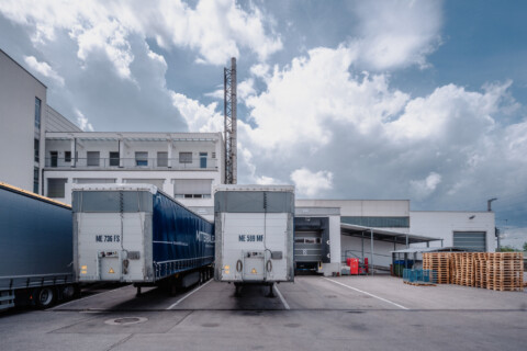 Lorries parked outside a warehouse under a partly cloudy sky.