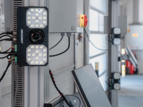 A mounted camera with LED lights attached to a wall in an industrial setting.