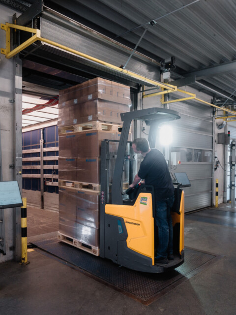 A forklift operating in a warehouse, navigating around stacked pallets in a spacious loading area.