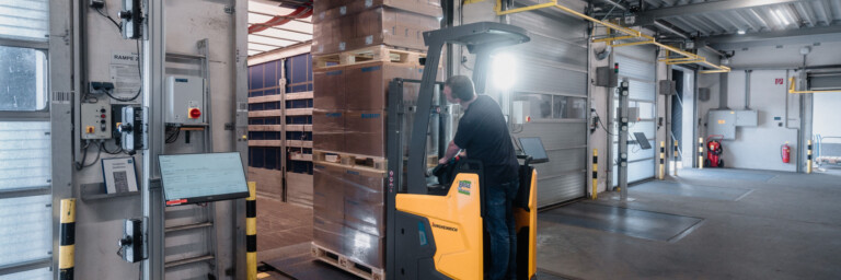 A forklift operating in a warehouse, navigating around stacked pallets in a spacious loading area.