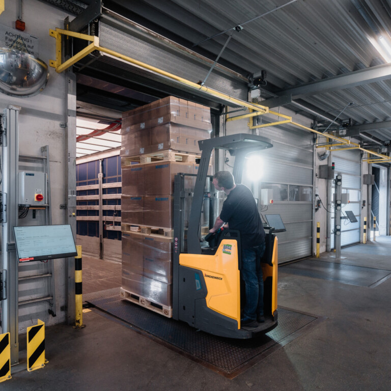 A forklift operating in a warehouse, navigating around stacked pallets in a spacious loading area.