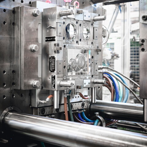 Nahaufnahme eines komplexen Spritzgusswerkzeugs mit zahlreichen Metallteilen und Kabeln in einer Produktionsanlage.