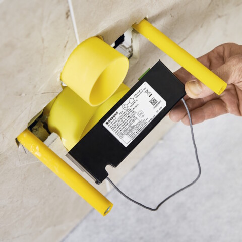 Eine Hand, die eine elektrische Anschlussdose mit gelben Leitungsrohren in einer Wand installiert.