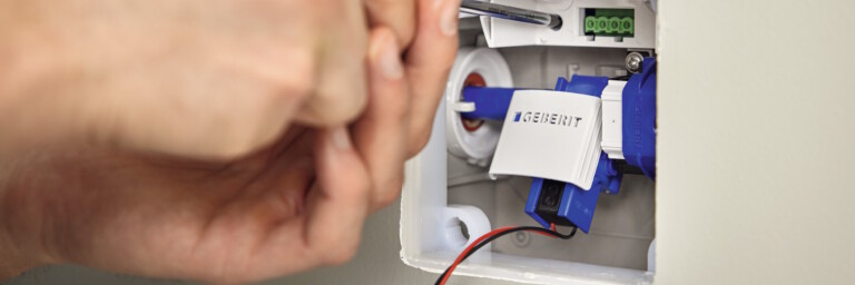 Eine Hand hält einen Schraubenzieher, mit dem sie über einem weissen Schalter arbeitet, der in eine weisse Wand eingelassen ist.