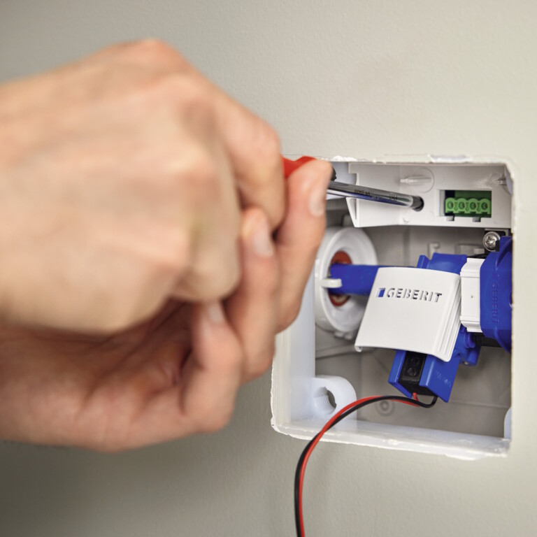 Eine Hand hält einen Schraubenzieher, mit dem sie über einem weissen Schalter arbeitet, der in eine weisse Wand eingelassen ist.