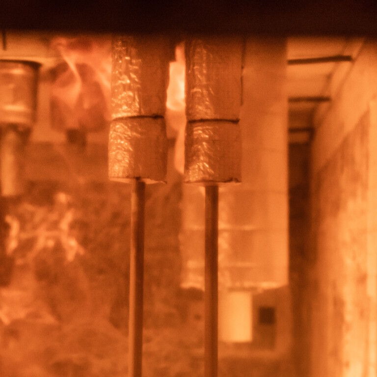Inside a furnace, pipes hang from the ceiling, the light is orange, and faint traces of smoke can be seen.
