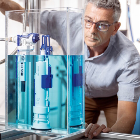 Ein Mann mit Brille, der ein transparentes Wasserbecken mit einem Füllventil beobachtet.