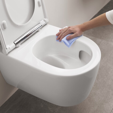 Eine Hand wischt mit einem blauen Tuch eine saubere, weisse, Toilette ab