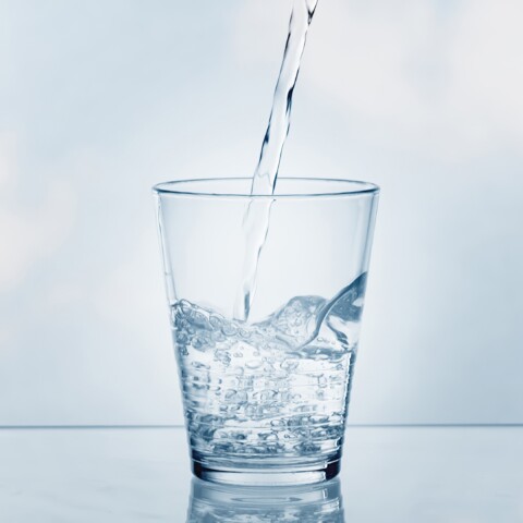 Wasser, das in ein klares Glas auf einer reflektierenden Oberfläche gegossen wird.