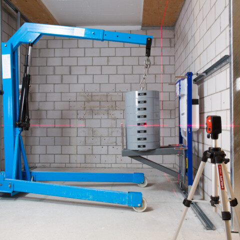 Lasttest an einer Sanitärinstallation für Wand-WCs mit einem blauen Motorlift und einem Laser-Nivelliergerät