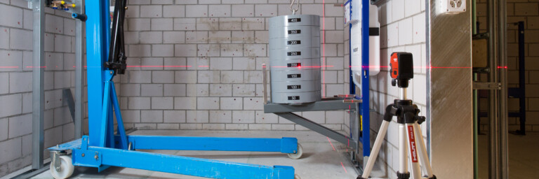 Lasttest an einer Sanitärinstallation für Wand-WCs mit einem blauen Motorlift und einem Laser-Nivelliergerät