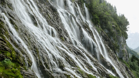Several waterfalls cascade down a steep, rocky cliff face, surrounded by green vegetation.