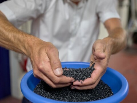 Hands of a person holding black plastic pellets from a blue bowl